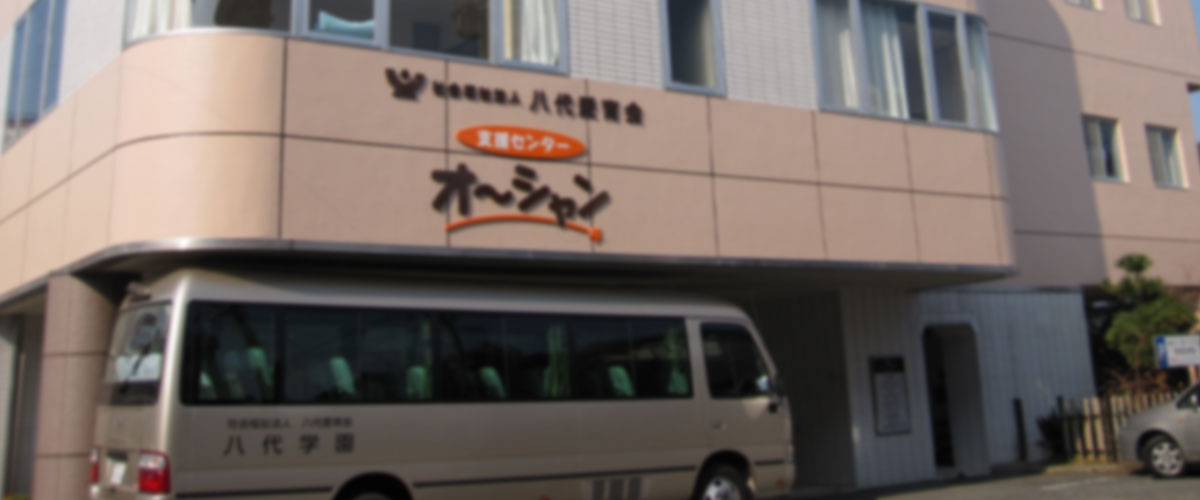 介護施設の玄関・車寄せ。施設名看板とリフト付き送迎車が見える